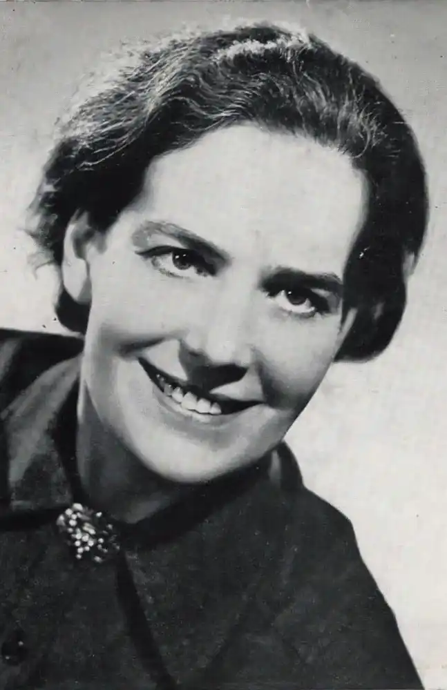 b&w photo taken in the 50s, possibly. white woman, smiling, in her 4os ddark haird, neat hair do. dark buttoned top, with a glittering brooch at her throat. Classic portrait of its time.